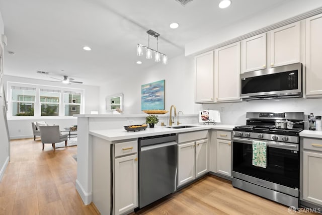 kitchen with light wood-type flooring, light countertops, appliances with stainless steel finishes, a peninsula, and a sink