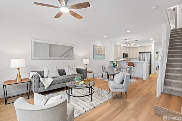 living room featuring baseboards, light wood-type flooring, stairs, recessed lighting, and a ceiling fan