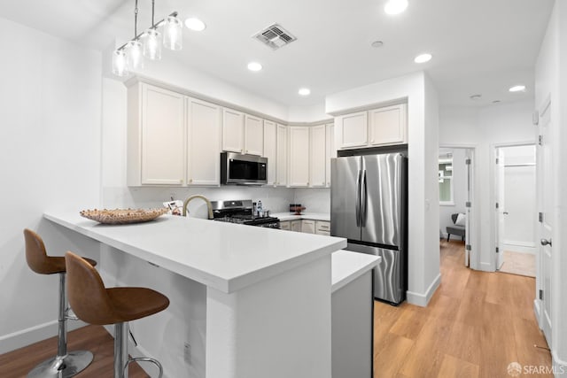 kitchen with visible vents, a breakfast bar area, light wood-type flooring, appliances with stainless steel finishes, and a peninsula