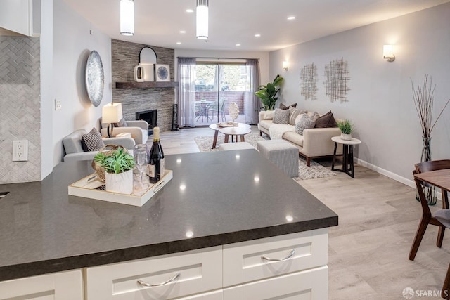 kitchen featuring decorative light fixtures, light hardwood / wood-style floors, decorative backsplash, white cabinetry, and a fireplace