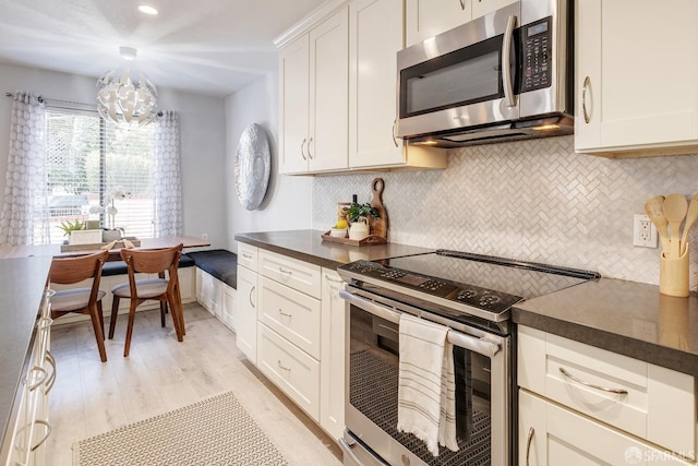 kitchen with white cabinetry, stainless steel appliances, a notable chandelier, light hardwood / wood-style flooring, and tasteful backsplash