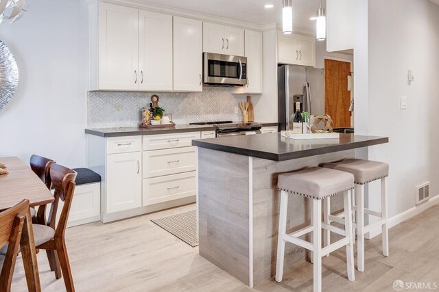 kitchen featuring decorative light fixtures, appliances with stainless steel finishes, a kitchen breakfast bar, and white cabinetry