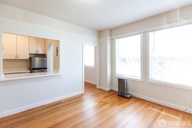 unfurnished living room with arched walkways, baseboards, radiator heating unit, and light wood-style flooring