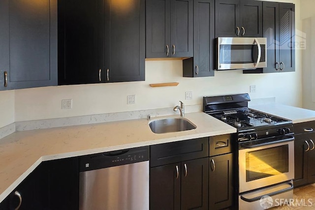 kitchen featuring a sink, light stone counters, dark cabinetry, and stainless steel appliances