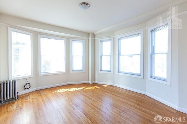 empty room with radiator heating unit, baseboards, and wood finished floors