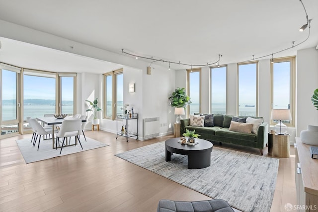 living area with radiator heating unit, wood finished floors, a water view, rail lighting, and expansive windows