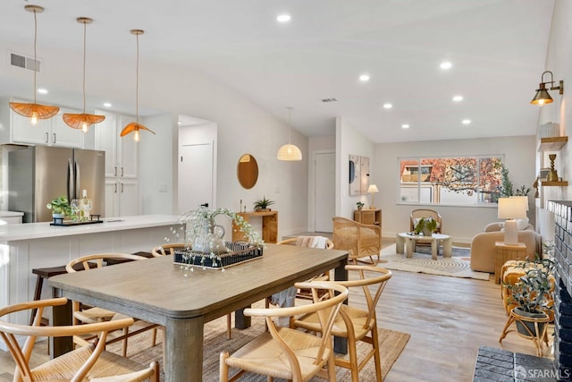 dining space with light hardwood / wood-style flooring, vaulted ceiling, and a brick fireplace