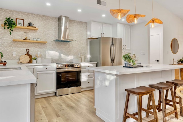 kitchen featuring wall chimney exhaust hood, stainless steel appliances, pendant lighting, white cabinets, and light hardwood / wood-style floors