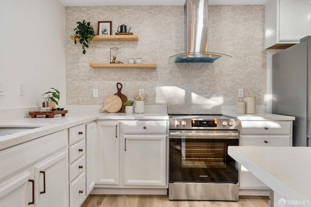 kitchen with appliances with stainless steel finishes, light stone counters, wall chimney range hood, light hardwood / wood-style flooring, and white cabinets