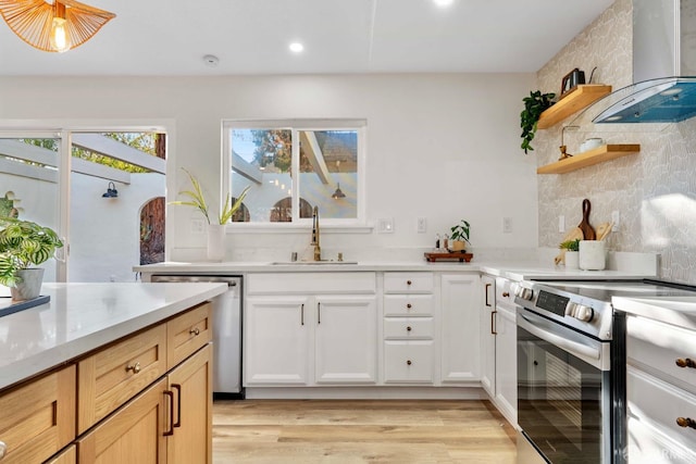 kitchen with wall chimney range hood, sink, light hardwood / wood-style flooring, appliances with stainless steel finishes, and white cabinetry