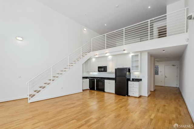 kitchen featuring light wood-type flooring, black appliances, a high ceiling, and white cabinets