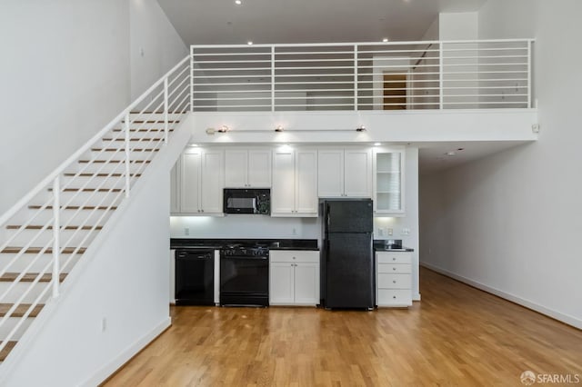 kitchen featuring a high ceiling, black appliances, light hardwood / wood-style floors, and white cabinetry