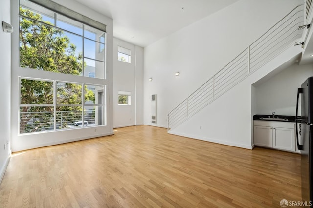 unfurnished living room featuring sink, light hardwood / wood-style floors, and a high ceiling