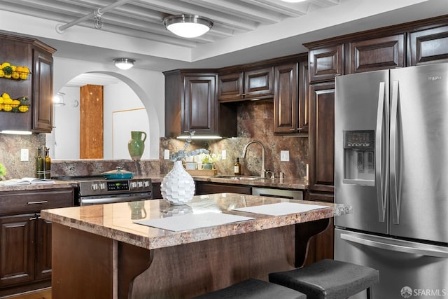 kitchen with a sink, a kitchen breakfast bar, a kitchen island, stainless steel appliances, and dark brown cabinets