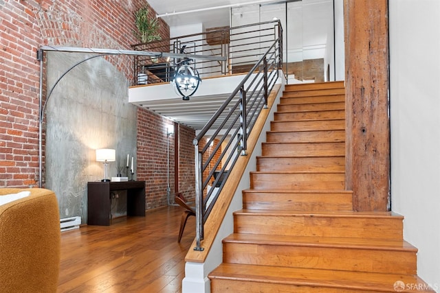 staircase with brick wall, a baseboard heating unit, a high ceiling, and wood finished floors