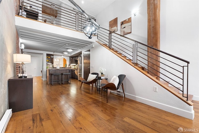 interior space featuring stairway, light wood-style floors, a high ceiling, baseboards, and baseboard heating