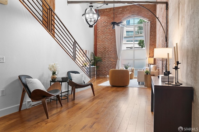 sitting room with light wood-type flooring, a notable chandelier, a high ceiling, brick wall, and baseboards