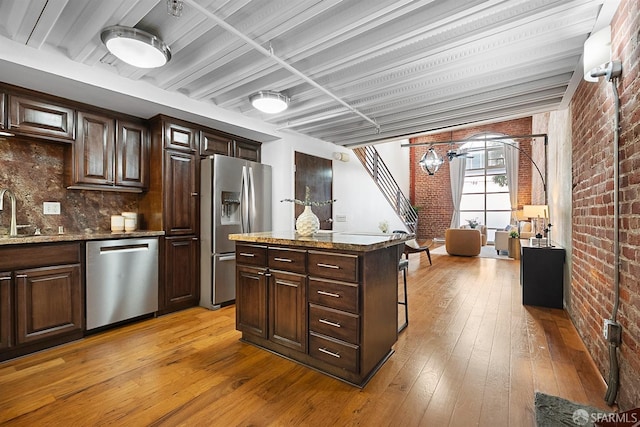 kitchen with brick wall, a kitchen island, appliances with stainless steel finishes, light wood-style floors, and a sink