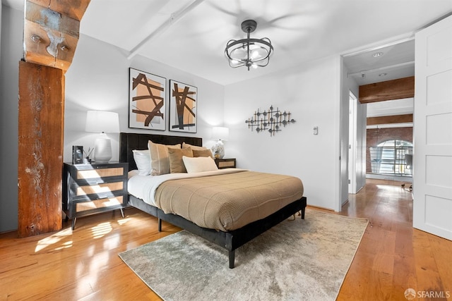 bedroom with beam ceiling, wood finished floors, and a chandelier