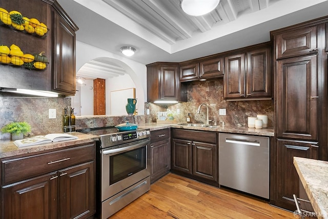 kitchen with a sink, stainless steel appliances, arched walkways, dark brown cabinetry, and light wood finished floors