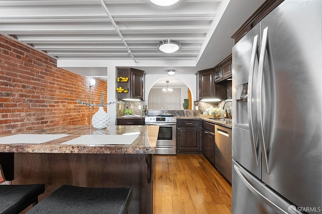 kitchen with dark brown cabinetry, appliances with stainless steel finishes, brick wall, and light wood-type flooring