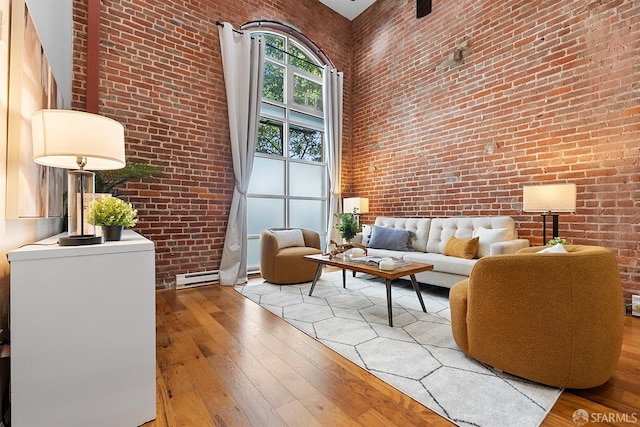 living area featuring light wood-type flooring, brick wall, and a towering ceiling