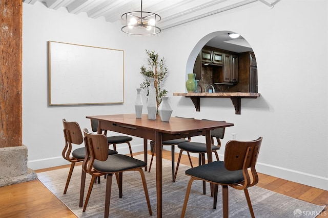 dining area with wood finished floors, baseboards, arched walkways, beamed ceiling, and a chandelier