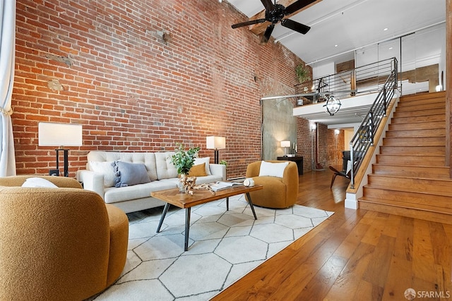 living area featuring hardwood / wood-style flooring, stairway, brick wall, and ceiling fan