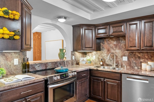 kitchen featuring a sink, tasteful backsplash, arched walkways, dark brown cabinetry, and appliances with stainless steel finishes