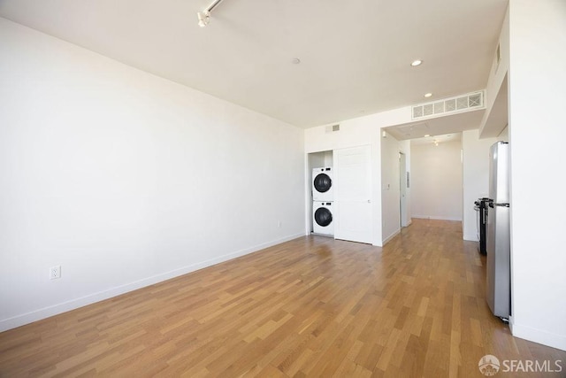 empty room featuring stacked washing maching and dryer and light hardwood / wood-style floors