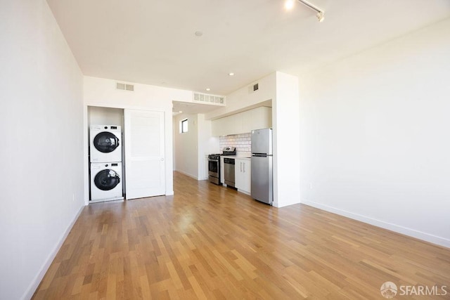 interior space with tasteful backsplash, stainless steel appliances, stacked washer / dryer, and light hardwood / wood-style floors