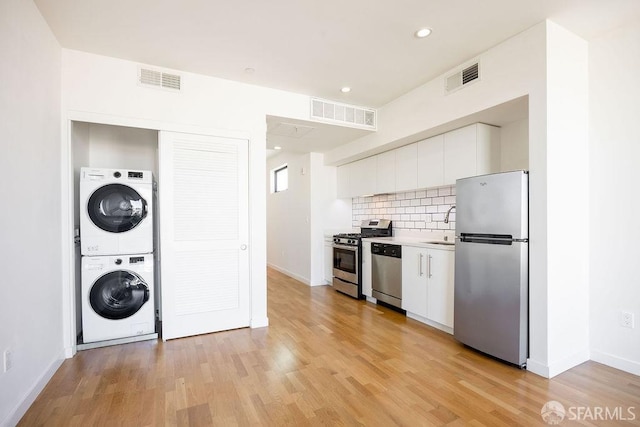 kitchen with white cabinetry, stainless steel appliances, stacked washer / drying machine, and light wood-type flooring