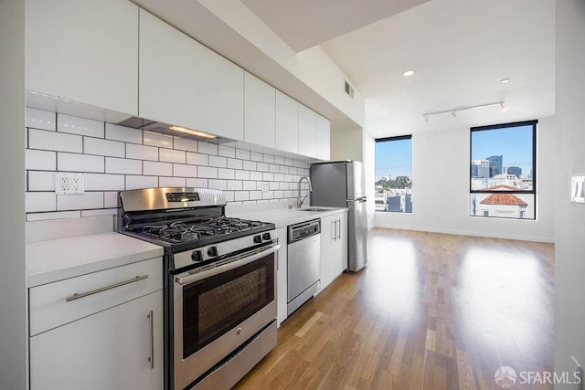 kitchen featuring decorative backsplash, light wood-type flooring, stainless steel appliances, sink, and white cabinets