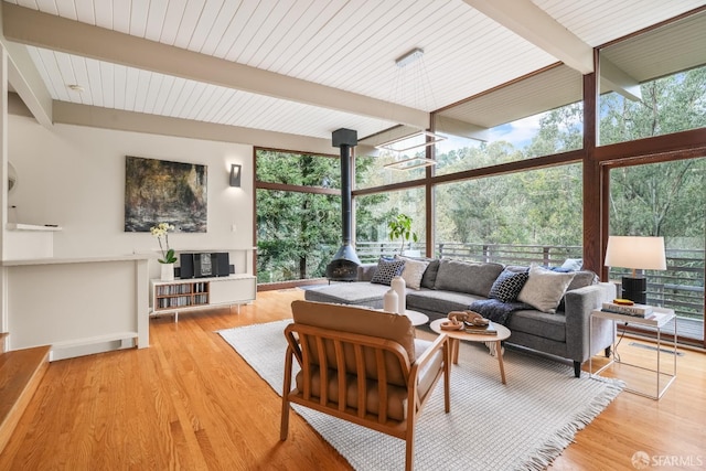 living room with a wall of windows, beam ceiling, wood finished floors, and a wood stove