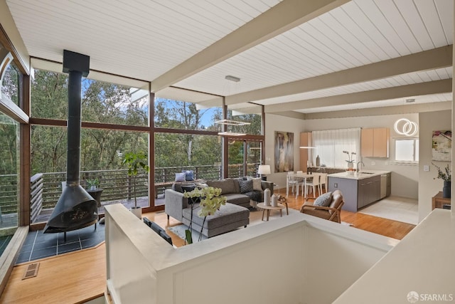 living area featuring beam ceiling, visible vents, a wall of windows, and a wood stove