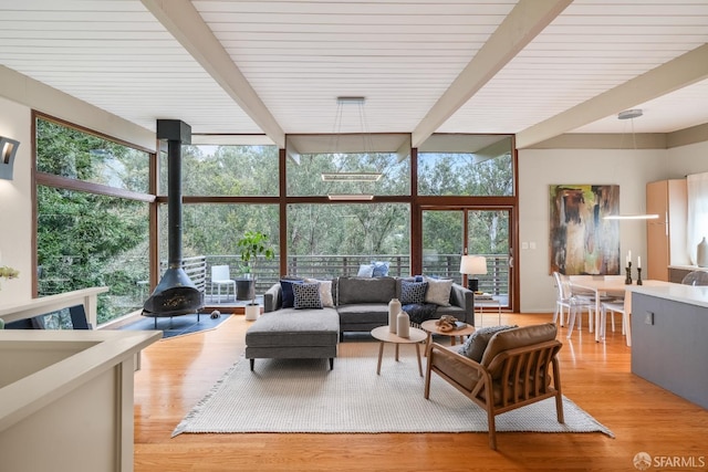 living area featuring beamed ceiling, light wood-style flooring, a wall of windows, and a wood stove