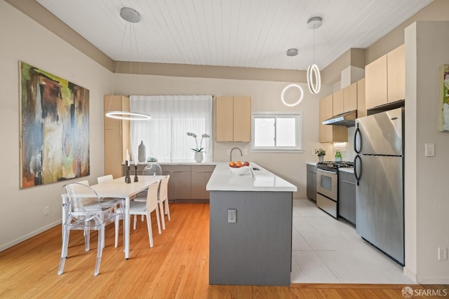 kitchen featuring a sink, under cabinet range hood, decorative light fixtures, stainless steel appliances, and light countertops