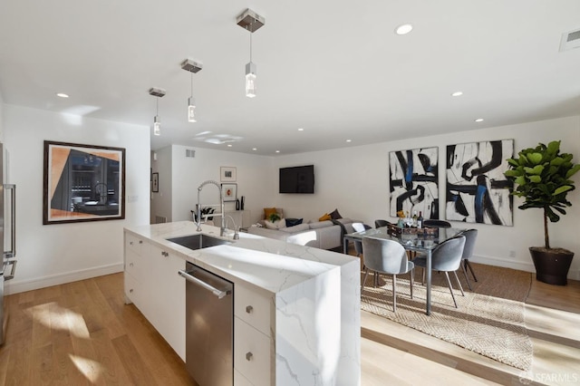 kitchen featuring dishwasher, a kitchen island with sink, sink, white cabinets, and decorative light fixtures