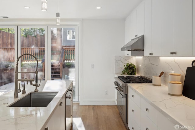 kitchen featuring light hardwood / wood-style floors, light stone counters, white cabinets, high end stove, and pendant lighting