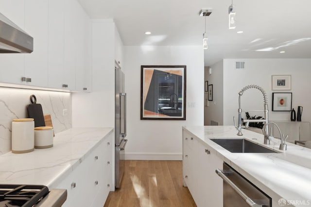 kitchen with light wood-type flooring, white cabinets, hanging light fixtures, wall chimney range hood, and appliances with stainless steel finishes