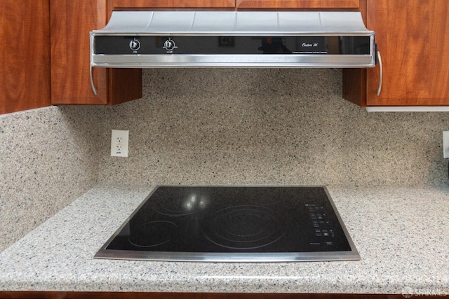 room details featuring tasteful backsplash, brown cabinetry, range hood, black electric cooktop, and light countertops