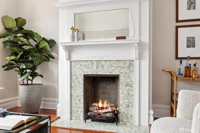 living area featuring a tile fireplace, baseboards, and wood finished floors