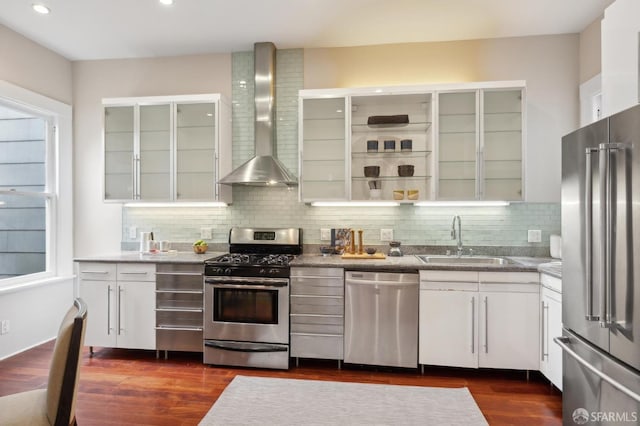 kitchen featuring appliances with stainless steel finishes, glass insert cabinets, white cabinets, a sink, and wall chimney range hood