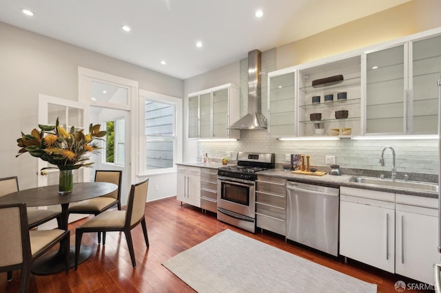 kitchen featuring glass insert cabinets, wall chimney range hood, appliances with stainless steel finishes, and open shelves