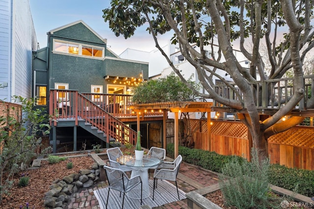 back house at dusk featuring a wooden deck and a patio area