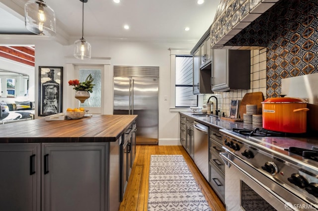 kitchen featuring pendant lighting, sink, wooden counters, high end appliances, and a center island