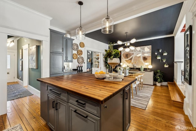 kitchen featuring hardwood / wood-style floors, butcher block counters, hanging light fixtures, ornamental molding, and a center island