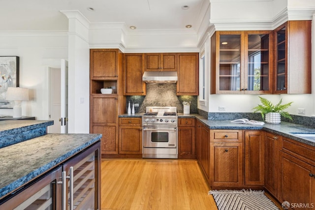 kitchen with high end stove, brown cabinets, beverage cooler, light wood-style floors, and under cabinet range hood