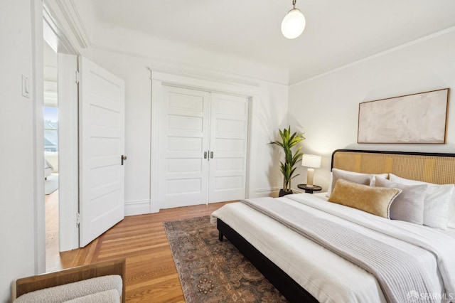 bedroom featuring light wood-style floors, crown molding, and a closet