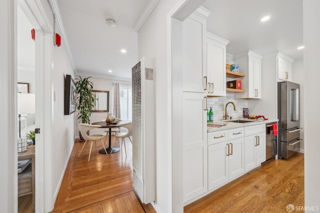 bar with high end refrigerator, light hardwood / wood-style floors, sink, white cabinetry, and ornamental molding